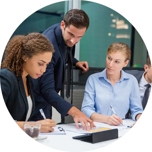 Three business professionals discussing documents at a table in an office setting.